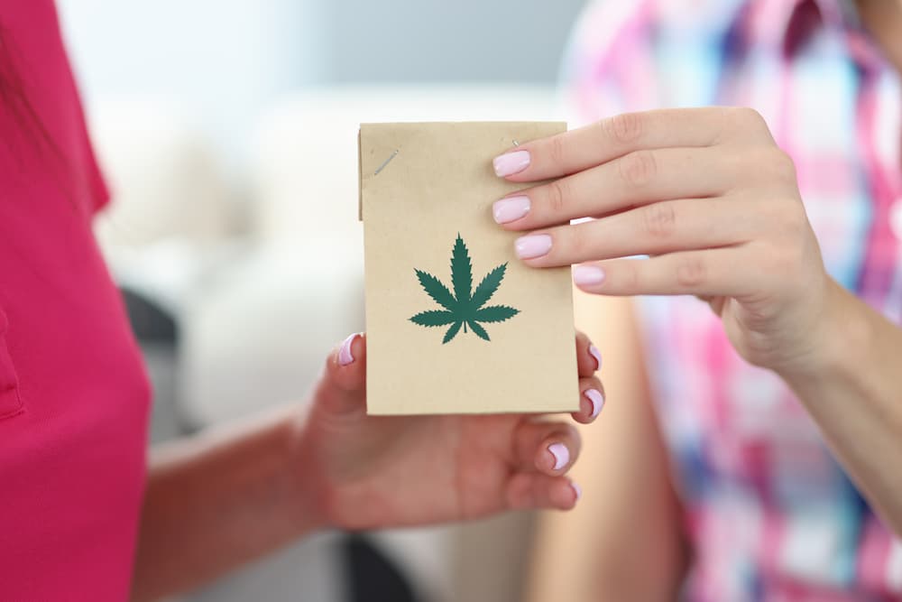 Image of two people passing a small bag with a weed leaf logo in it.